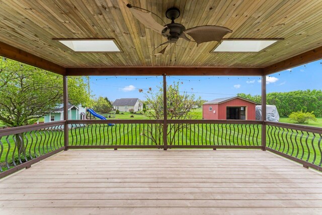 deck with a playground, ceiling fan, a shed, a yard, and an outbuilding