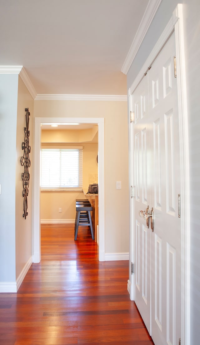 corridor with dark wood-type flooring, baseboards, and ornamental molding