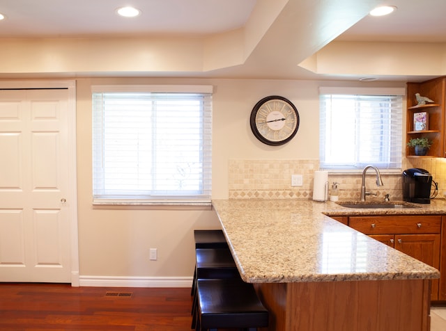kitchen featuring a sink, brown cabinets, light stone counters, backsplash, and recessed lighting
