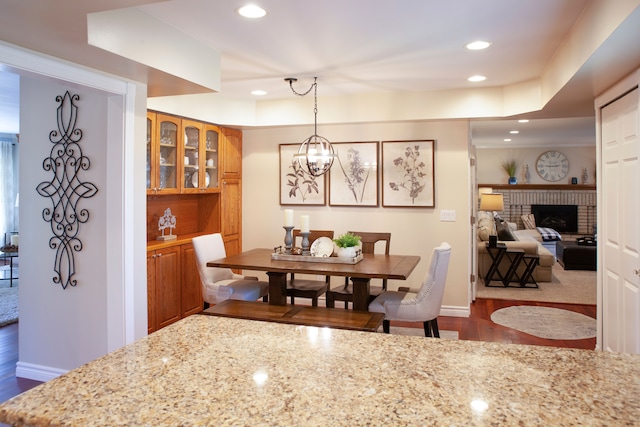 dining area with dark wood-type flooring, recessed lighting, a brick fireplace, baseboards, and a chandelier