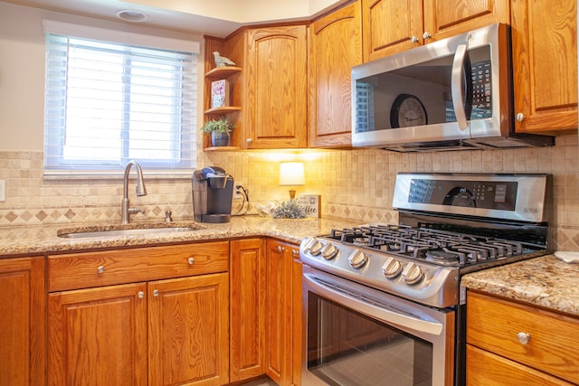 kitchen with stainless steel appliances, a sink, decorative backsplash, light stone counters, and plenty of natural light
