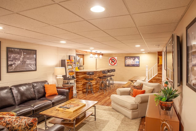 living area with wood finished floors, a dry bar, concrete block wall, a paneled ceiling, and stairway