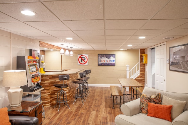 indoor wet bar featuring wood finished floors, concrete block wall, a paneled ceiling, recessed lighting, and baseboards