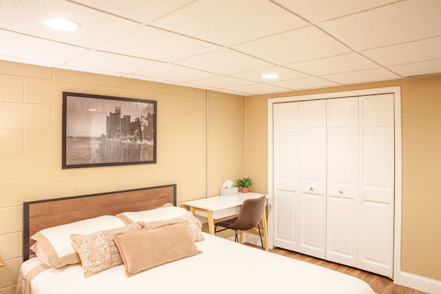 bedroom featuring wood finished floors, a closet, a paneled ceiling, concrete block wall, and recessed lighting