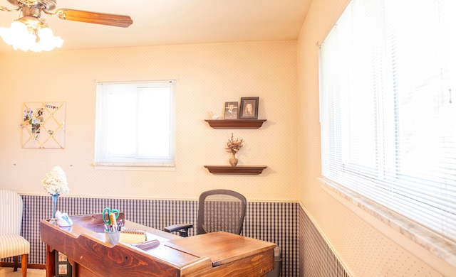 home office featuring wallpapered walls, wainscoting, and a ceiling fan