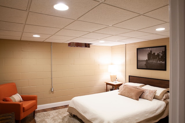 bedroom with wood finished floors, recessed lighting, a paneled ceiling, and baseboards