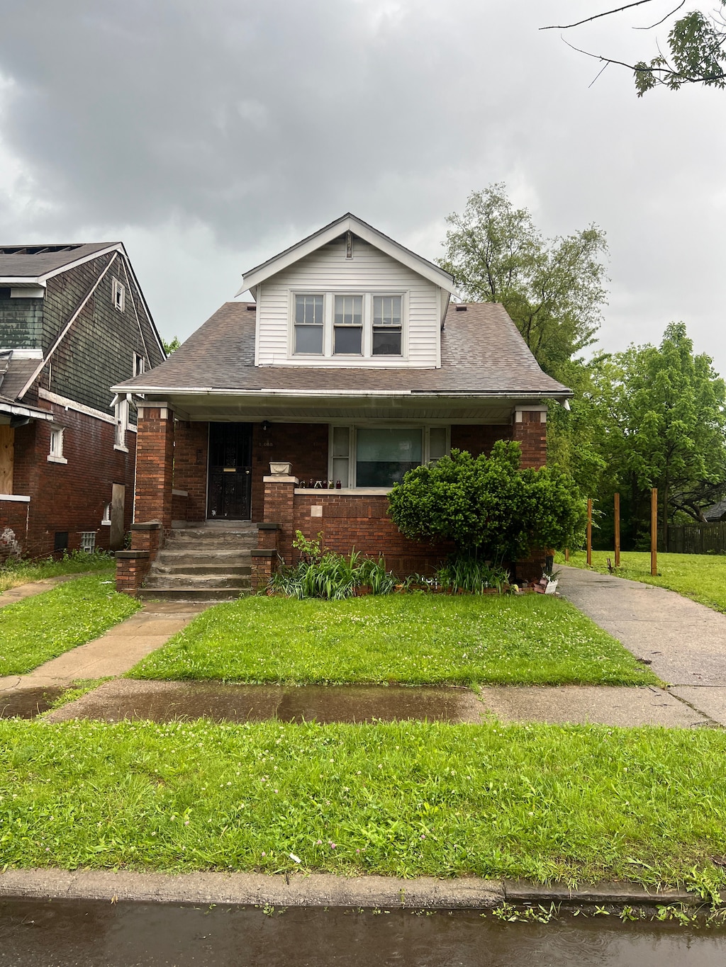12088 Promenade St, Detroit, MI 48213 - view of front facade featuring a front yard, covered porch, brick siding, and a shingled roof