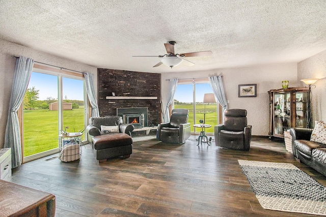 living area with wood-type flooring, a textured ceiling, ceiling fan, and a large fireplace