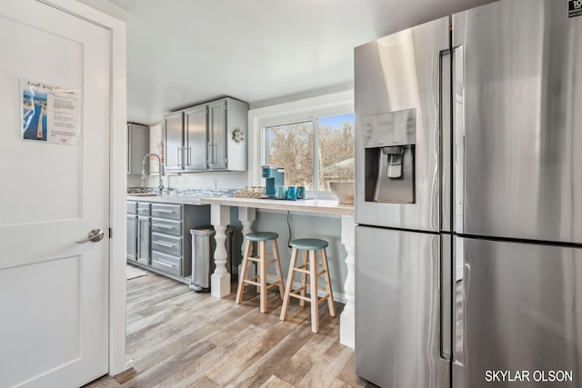 kitchen with stainless steel fridge with ice dispenser, light wood-type flooring, a kitchen breakfast bar, light countertops, and gray cabinetry