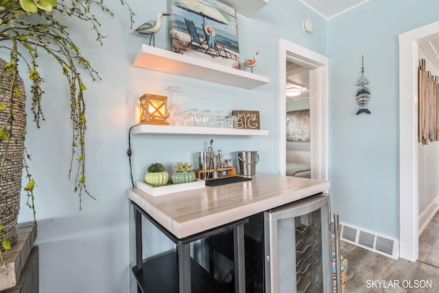 indoor dry bar with beverage cooler, wood finished floors, crown molding, and baseboards
