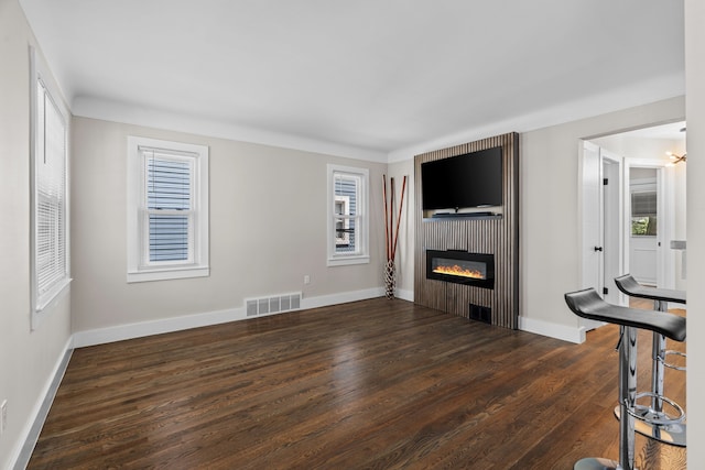 unfurnished living room featuring healthy amount of natural light, a glass covered fireplace, wood finished floors, and baseboards