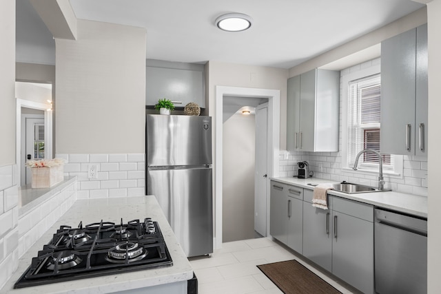 kitchen featuring stainless steel appliances, gray cabinetry, a sink, and decorative backsplash