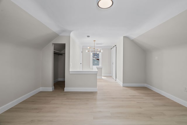 additional living space with a chandelier, light wood finished floors, baseboards, and vaulted ceiling