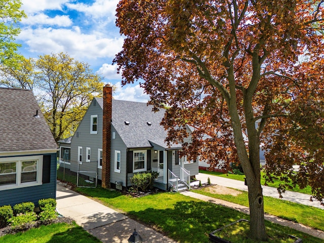 view of front of home with a shingled roof, a chimney, and a front lawn