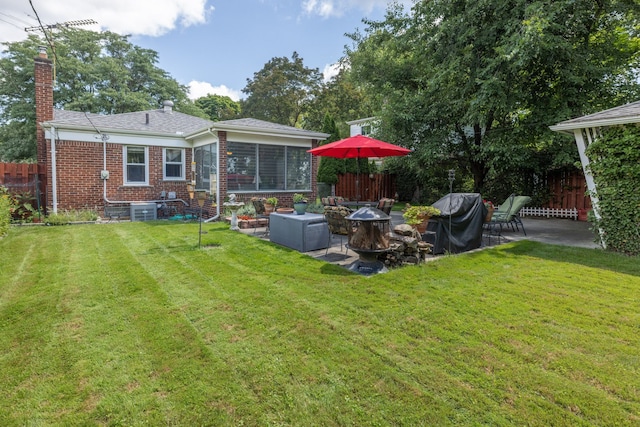 back of house with a chimney, an outdoor fire pit, brick siding, a patio, and a sunroom