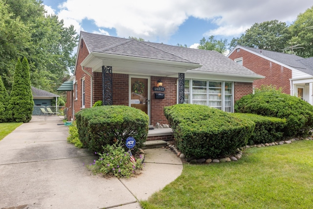 bungalow featuring brick siding, roof with shingles, and a front lawn