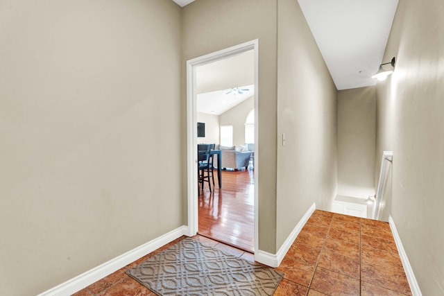 hall featuring an upstairs landing, baseboards, and vaulted ceiling