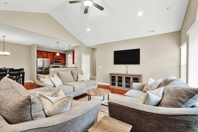 living room featuring vaulted ceiling, a chandelier, a ceiling fan, light wood finished floors, and baseboards