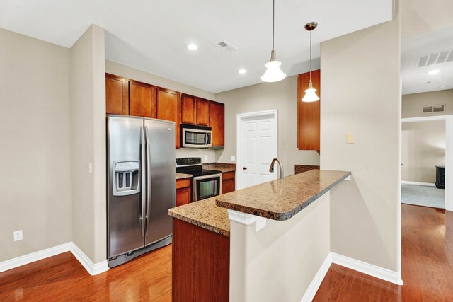kitchen featuring appliances with stainless steel finishes, a peninsula, baseboards, wood finished floors, and pendant lighting