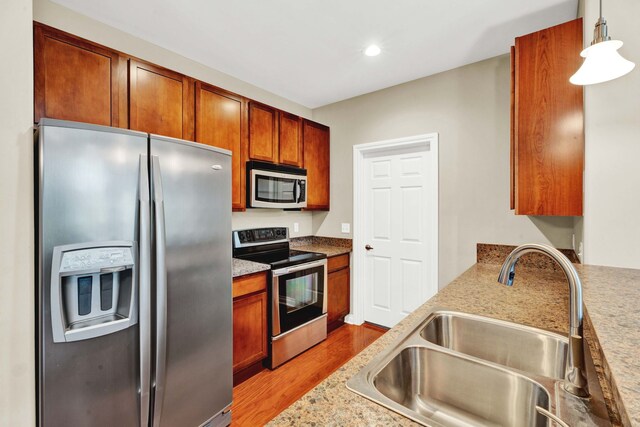 kitchen with stainless steel appliances, a sink, light wood-type flooring, brown cabinets, and recessed lighting