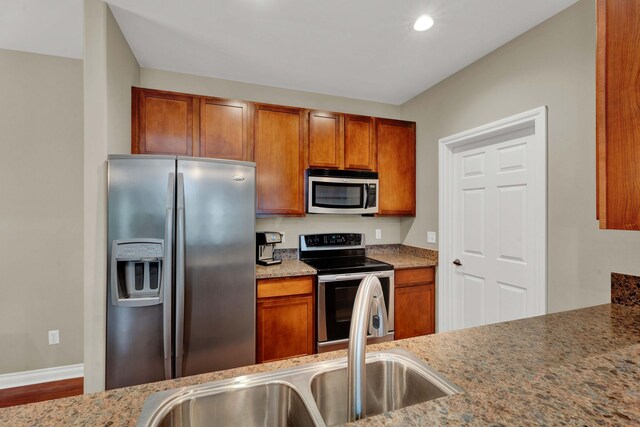 kitchen with appliances with stainless steel finishes, a sink, brown cabinetry, wood finished floors, and recessed lighting