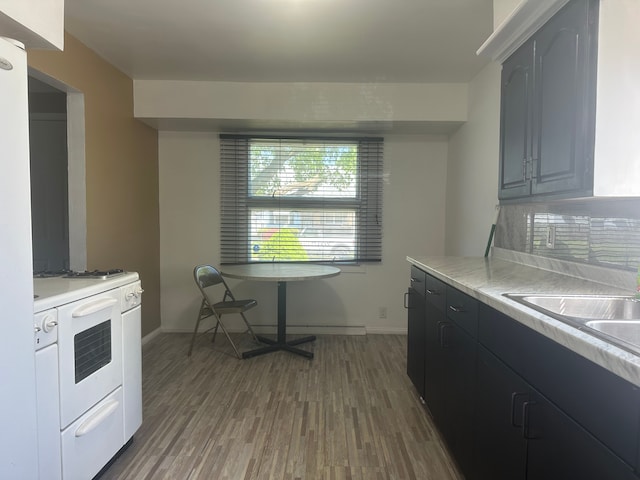 kitchen with light countertops, wood finished floors, white range with gas cooktop, baseboards, and a sink