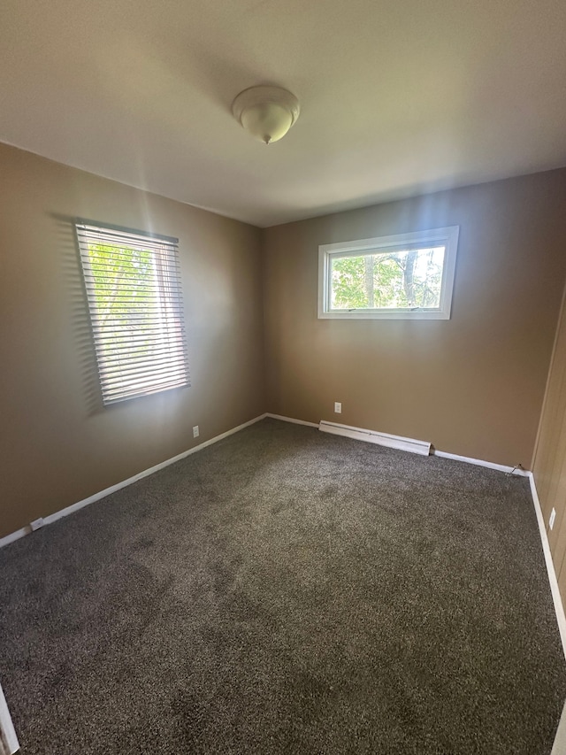 spare room featuring dark carpet, baseboards, and a baseboard heating unit