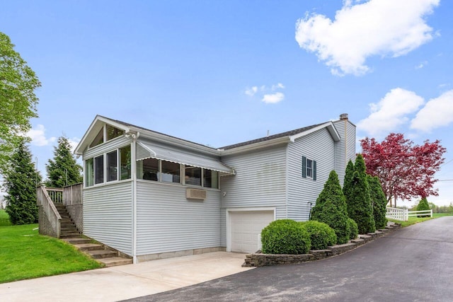 view of side of property with stairway, driveway, an attached garage, a sunroom, and a chimney