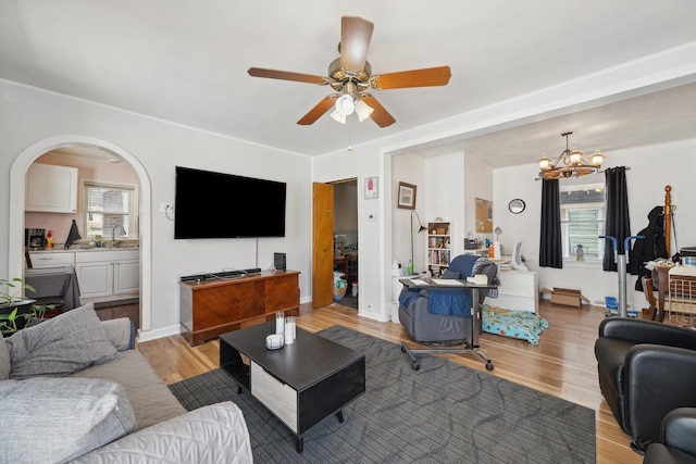living area featuring a ceiling fan, a chandelier, light wood-style floors, and arched walkways
