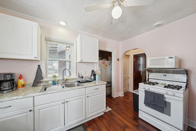 kitchen with white appliances, a sink, arched walkways, a textured ceiling, and white cabinets