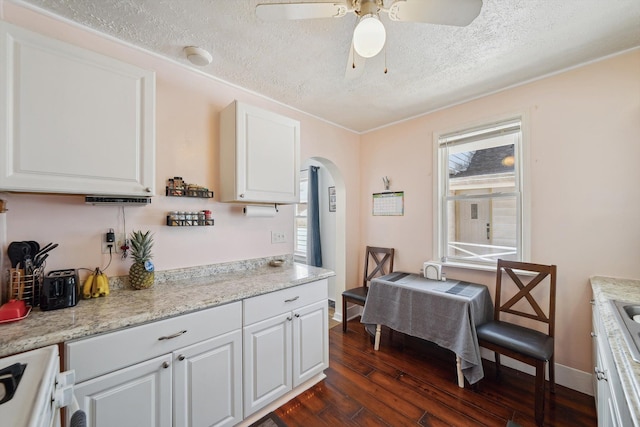 kitchen with a textured ceiling, dark wood-style floors, arched walkways, stove, and white cabinets