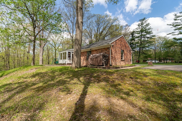 view of side of property featuring a sunroom, brick siding, and a yard