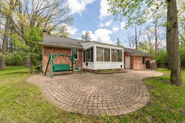 back of house featuring brick siding, a sunroom, a chimney, and a lawn
