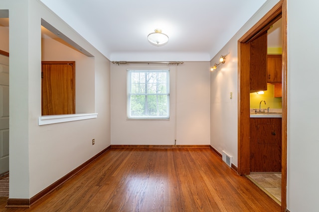spare room with wood finished floors, a sink, and baseboards