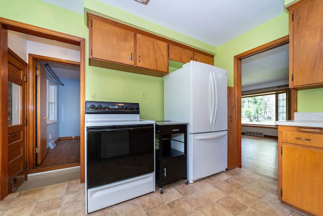kitchen featuring electric stove, freestanding refrigerator, light countertops, brown cabinetry, and stone finish floors