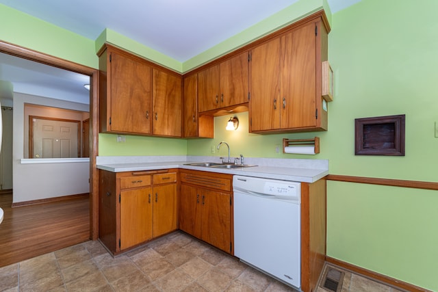 kitchen with dishwasher, a sink, light countertops, baseboards, and brown cabinetry