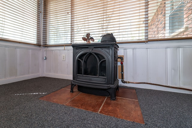 detailed view of a wood stove, carpet floors, a decorative wall, and a wainscoted wall