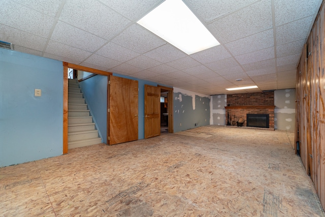 finished below grade area featuring a brick fireplace, stairs, and a drop ceiling