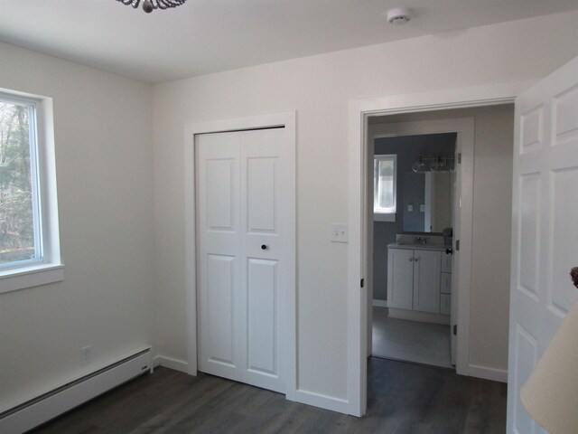 1192 Little Creek Rd SE, Alger, MI 48610 - unfurnished bedroom with baseboard heating, dark wood-type flooring, a closet, and baseboards