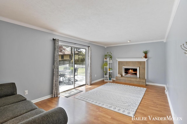 living area with wood finished floors, a fireplace, baseboards, and crown molding