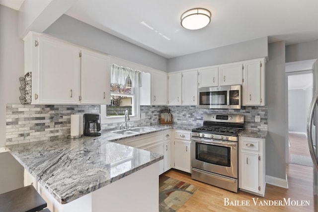 kitchen featuring appliances with stainless steel finishes, a peninsula, a sink, light stone countertops, and white cabinets