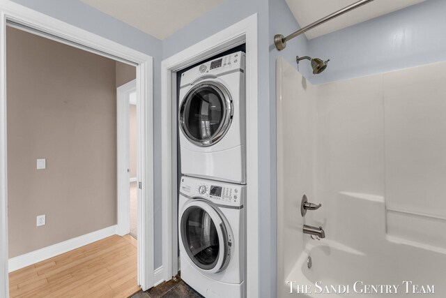 clothes washing area with stacked washer / dryer, baseboards, and wood finished floors