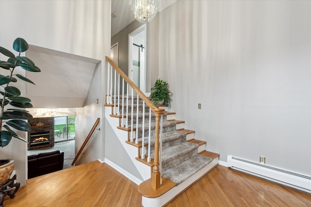 9669 Norman Rd, Clarkston, MI 48348 - staircase featuring baseboard heating, baseboards, wood finished floors, a stone fireplace, and a chandelier