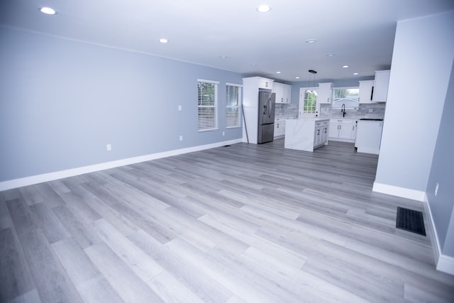 unfurnished living room with recessed lighting, baseboards, light wood-style flooring, and a sink