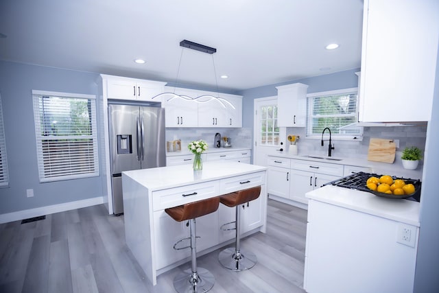 kitchen featuring stainless steel refrigerator with ice dispenser, a sink, a kitchen island, light wood-style flooring, and recessed lighting