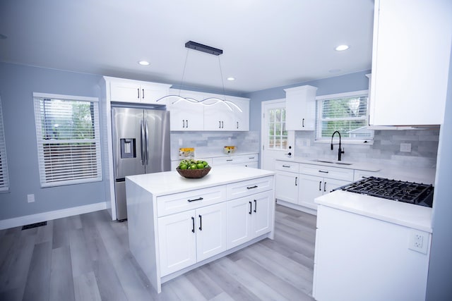 kitchen with stainless steel refrigerator with ice dispenser, a sink, light wood-style floors, a center island, and light countertops