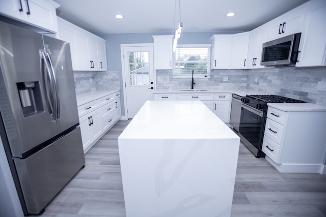 kitchen featuring appliances with stainless steel finishes, a sink, light wood-type flooring, tasteful backsplash, and light countertops