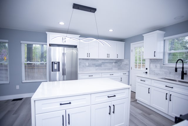 kitchen with stainless steel refrigerator with ice dispenser, a sink, light wood finished floors, decorative backsplash, and recessed lighting