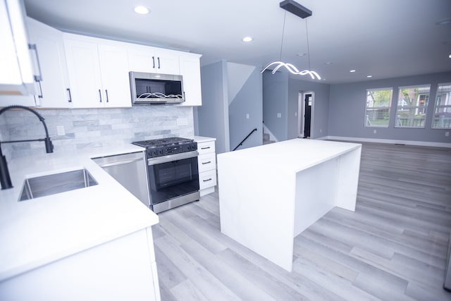 kitchen with appliances with stainless steel finishes, a sink, a center island, white cabinetry, and light wood-style flooring