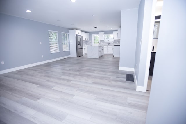 unfurnished living room featuring recessed lighting, baseboards, light wood-style flooring, and a sink